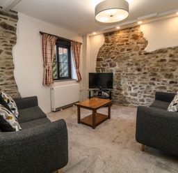 A living room with two grey sofas and a wooden coffee table in front of a stone wall with a television at Honey Bee Cottage in Bradworthy