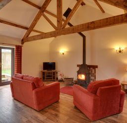 A living room with two red sofas a wood burning stove a tv and wooden beams at Woodpecker Cottage Bradworthy near Bude