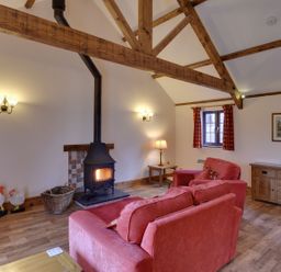 A sitting room with wooden beams red sofas a wood burner and wooden furniture at Woodpecker Cottage in Bradworthy near Bude