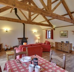 A living room with wooden beams a red sofa wood burning stove dining table with cups and plates at Woodpecker Cottage Bradworthy near Bude