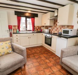 A kitchen with white cabinets two armchairs and a window with red curtains at Wagtail in Bradworthy near Bude