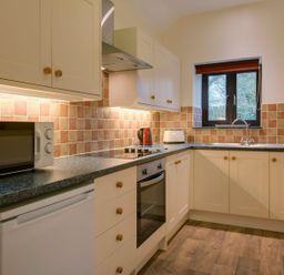 A kitchen with white cabinets a microwave oven electric stovetop toaster kettle and a window at Jenny Wren in Bradworthy