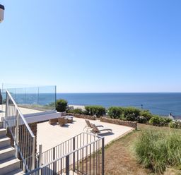 An outdoor terrace with lounge chairs and wicker furniture overlooking the sea at Boscregan in Porthleven