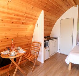 A small wooden room with a kitchenette a dining table with chairs and a bed at Lovesome Pod Lovesome Hill near Northallerton