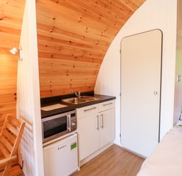 A small kitchenette with a microwave fridge and sink next to a door and a bed at Lovesome Pod Lovesome Hill near Northallerton