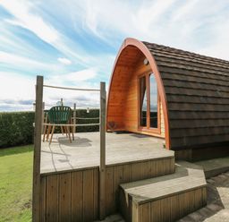 A wooden pod with a curved roof and a deck with a table and chair outside at Lovesome Pod Lovesome Hill near Northallerton