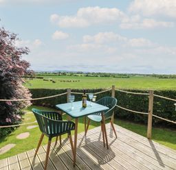 A deck with table and two chairs overlooking green fields and trees at Lovesome Pod Lovesome Hill near Northallerton