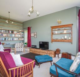 A living room with bookshelves chairs and a television at Plas Newydd in Llanfaelog near Rhosneigr