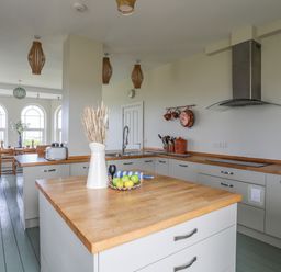 A kitchen with a wooden countertop island and dining area with wooden chairs and arched windows at Plas Newydd Llanfaelog near Rhosneigr
