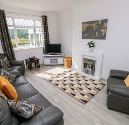 A living room with grey leather sofas a patterned rug a TV on a stand and a fireplace at Garth in Pen-y-bryn near Cardigan