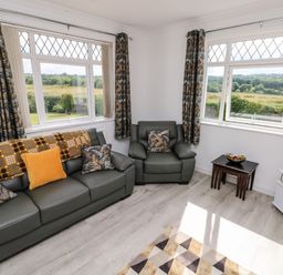 A living room with green sofas, patterned cushions, dark curtains, small tables, and a television at Garth in Pen-y-bryn near Cardigan