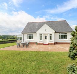 A white house with a dark roof and a patio with chairs and a table on a lawn at Garth in Pen-y-bryn near Cardigan