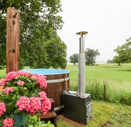 An outdoor hot tub next to wooden steps and pink flowers overlooking a grassy field at The Lazy Mare by The Water Admaston near Abbots Bromley