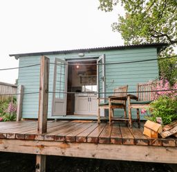 A wooden deck with two chairs and a flower pot outside a light blue cabin at The Lazy Mare by The Water in Admaston near Abbots Bromley