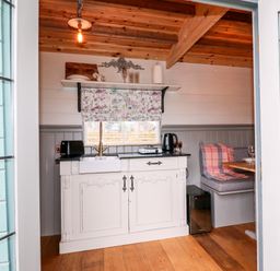 A small kitchen area with a white cabinet sink toaster kettle and a built in dining bench at The Lazy Mare by The Water in Admaston near Abbots Bromley