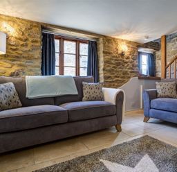 A living room with two gray sofas stone walls wooden window frames and a staircase at Hollytree Cottage in Hook Norton