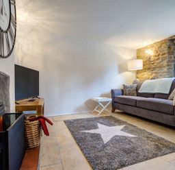 A living room with a sofa a rug with a star a fireplace and a wall clock at Hollytree Cottage in Hook Norton