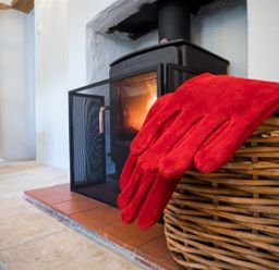 A wood burning stove with fire guard a wicker basket and red gloves at Hollytree Cottage in Hook Norton