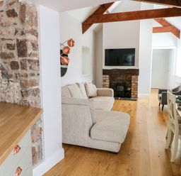 A living room with a beige sofa a wall-mounted TV and a dining table with chairs at Ramsey Cottage in Milford Haven