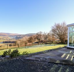 A backyard with a glass conservatory and bench overlooking fields and hills at Ty Twmp Tump Cottage in Tal-Y-Bont-On-Usk