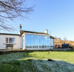 A white cottage with a glass sunroom and green lawn in front at Ty Twmp Tump Cottage in Tal-Y-Bont-On-Usk