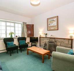 A living room with green carpet two armchairs a wooden coffee table and a fireplace at Ty Twmp Tump Cottage in Tal-Y-Bont-On-Usk