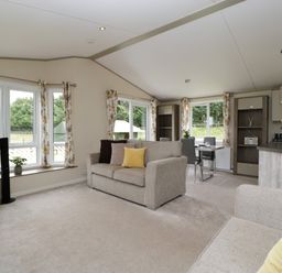 A living room with two beige sofas a dining table and chairs and a kitchen area at Hill View Lilac Lodge in Wareham