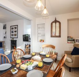 A dining room with wooden table set with plates and juice glasses and a living area with chairs and a fireplace at Silva in Penmon