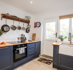 A kitchen with pots hanging on a rack a stove a sink and a door with windows at Silva in Penmon