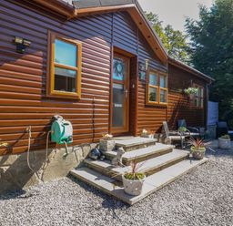 Exterior of a wooden house with steps leading to a door surrounded by planters and outdoor seating at RoseGrace Lodge in Auchterarder