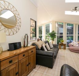 A living room with a wooden sideboard black leather sofa round pink chair and large windows at RoseGrace Lodge in Auchterarder