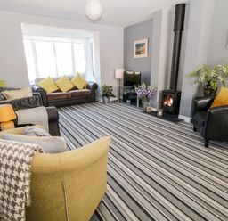 A living room with striped carpet a wood stove black armchair two sofas and a yellow armchair at Seagull Cottage in Bude