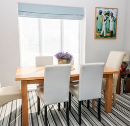 A dining room with a wooden table surrounded by six chairs and a flower centerpiece at Seagull Cottage in Bude