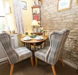 A dining area with two plaid chairs and a round wooden table set with bowls and cutlery at Coln Cottage in Stow-On-The-Wold