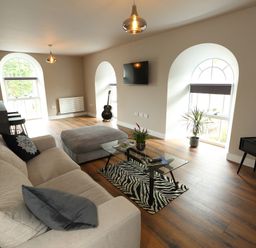 A living room with a sofa ottoman glass coffee table and guitar at The Poppy Fields Abode in Dyserth