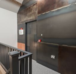 A hallway with a black railing a door and industrial style dark metal wall panels at The Sigma Penthouse in Dyserth