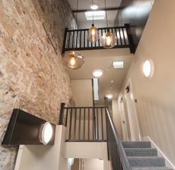 A stairway with carpeted steps and black railings next to a brick wall and hanging light fixtures at The Sigma Penthouse in Dyserth