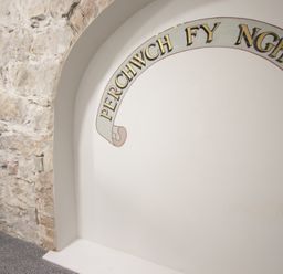 An interior wall with stone on one side and a white arched niche with text at The Sigma Penthouse in Dyserth
