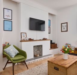 A living room with a green chair a wooden coffee table with flowers and a wall-mounted TV at Saltwater Cottage in Babbacombe