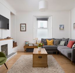A living room with a gray sectional sofa with colorful pillows a wooden coffee table with flowers and two green armchairs at Saltwater Cottage in Babbacombe