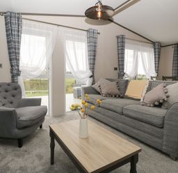 A living room with a grey sofa and armchair a wooden coffee table with flowers and plaid curtains at 14 Fairways in Burnham-On-Sea