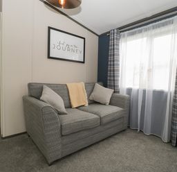 A living room with a grey sofa cushions blanket plaid curtains and a framed quote at 14 Fairways in Burnham-On-Sea