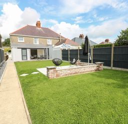 A backyard with green grass a paved walkway black fence two black chairs and a house in the background at Larkhill in Tenby