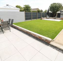 A backyard with tiled patio table and chairs a lawn a paved seating area and a garden shed at Larkhill in Tenby