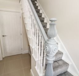 A staircase with grey carpet and a white painted banister next to a closed white door at Larkhill in Tenby