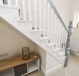 A staircase with white balusters and a gray handrail with a small wooden cabinet underneath at Larkhill in Tenby