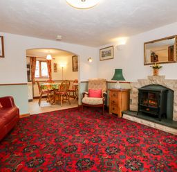 A living room with a red patterned carpet a leather sofa armchair fireplace and a dining table seen through an archway at Rose Cottage Burneside