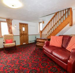 A living room with a red sofa and patterned carpet at Rose Cottage in Burneside