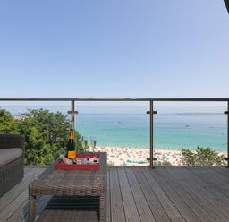 A balcony with wicker furniture a table with champagne glasses and bottle overlooking a beach and sea at Crystal Bay in St Ives