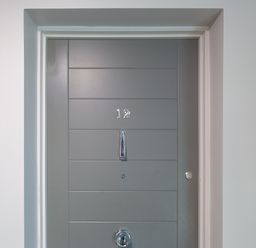 A gray door with the number 12 a door knocker a peephole and a lock in a white wall at Crystal Bay in St Ives